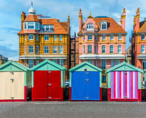 Brightly coloured beach huts in a row on Hovce beach, with to Regency style buildings sitting behind