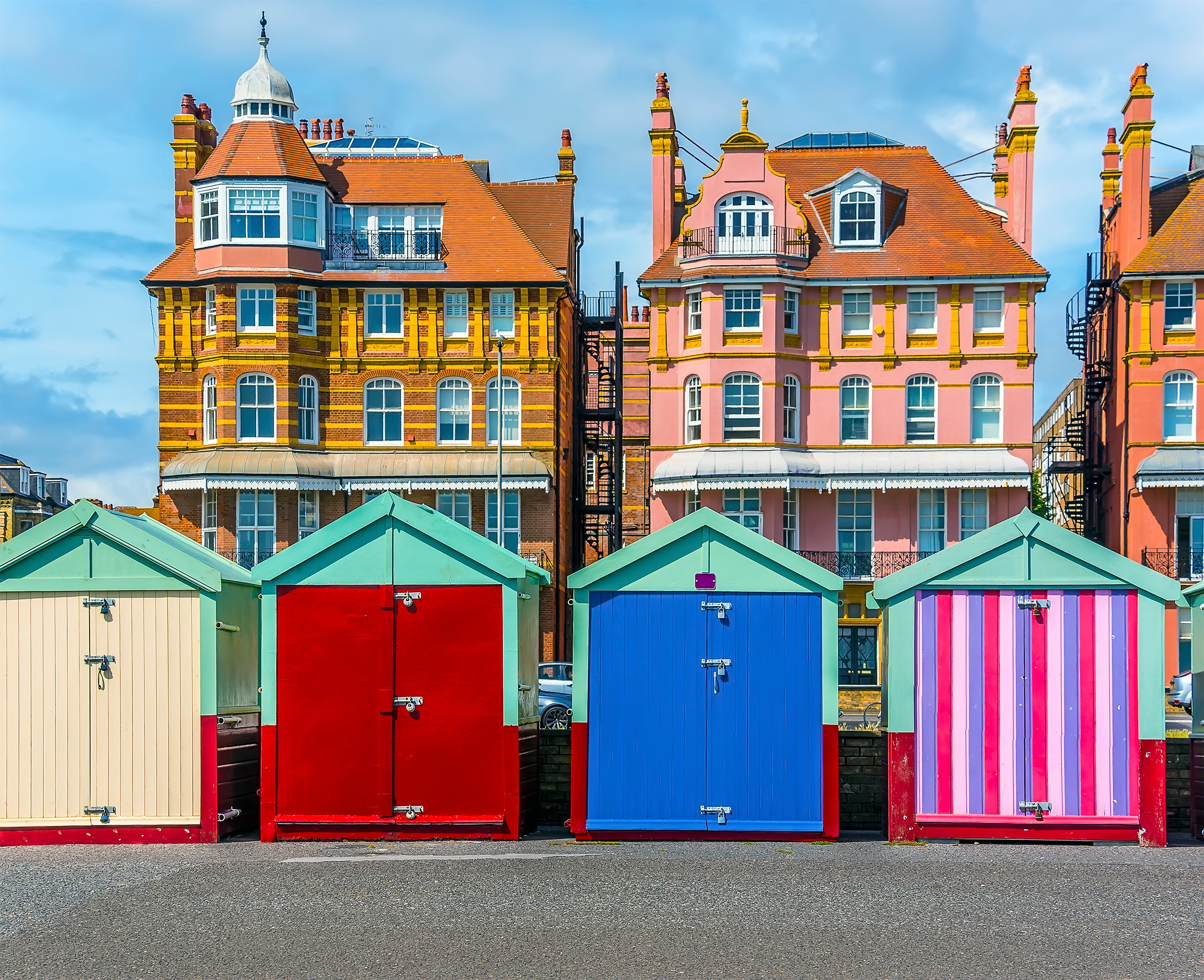 Brightly coloured beach huts in a row on Hovce beach, with to Regency style buildings sitting behind
